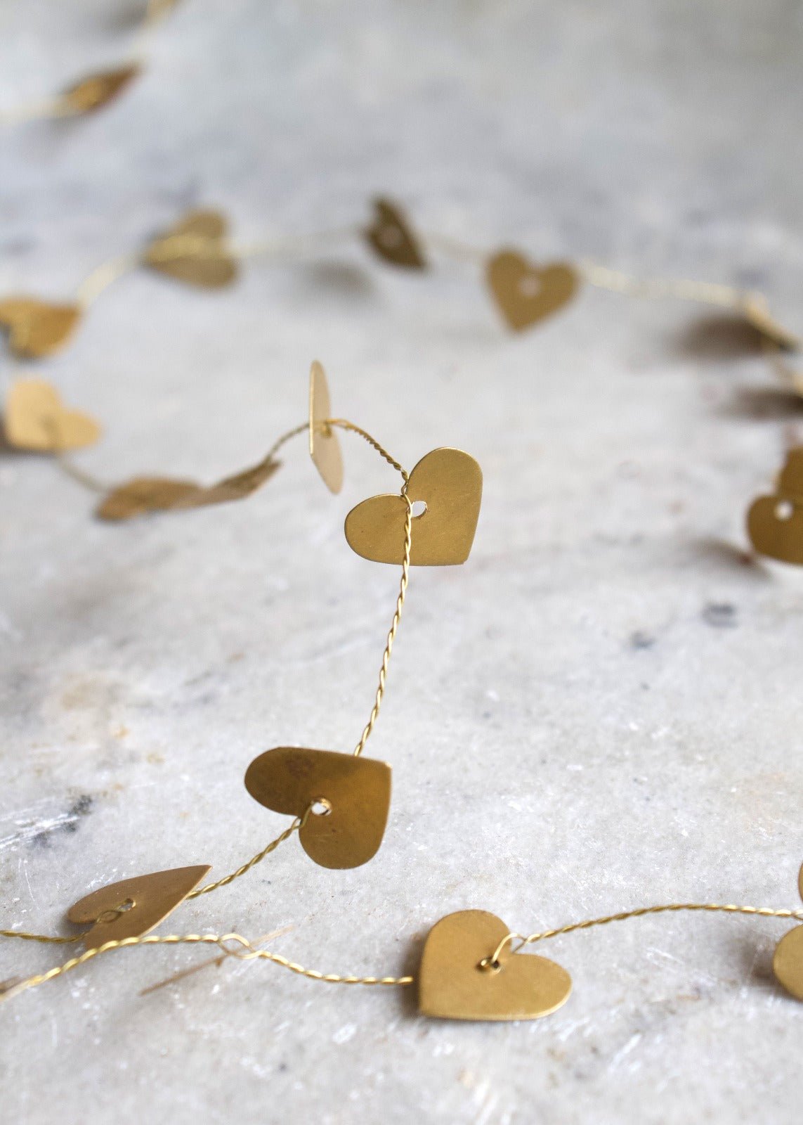 Brass heart garland with small golden hearts on twisted wire, displayed on a light stone surface.