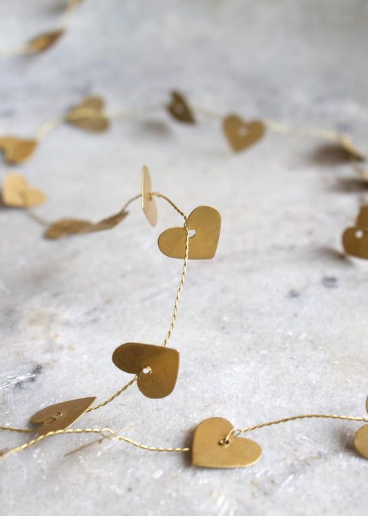 Brass heart garland with small golden hearts on twisted wire, displayed on a light stone surface.