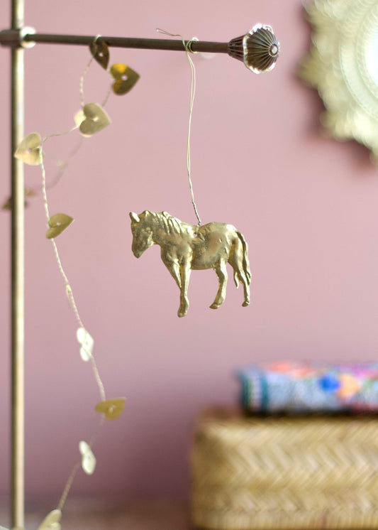 Gold horse ornament hanging from a rod with a pink wall in the background