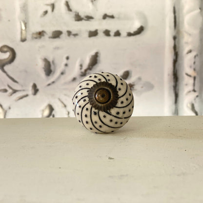 A black and white spiral patterned furniture knob with a visible center fastening mechanism, placed against a textured background.