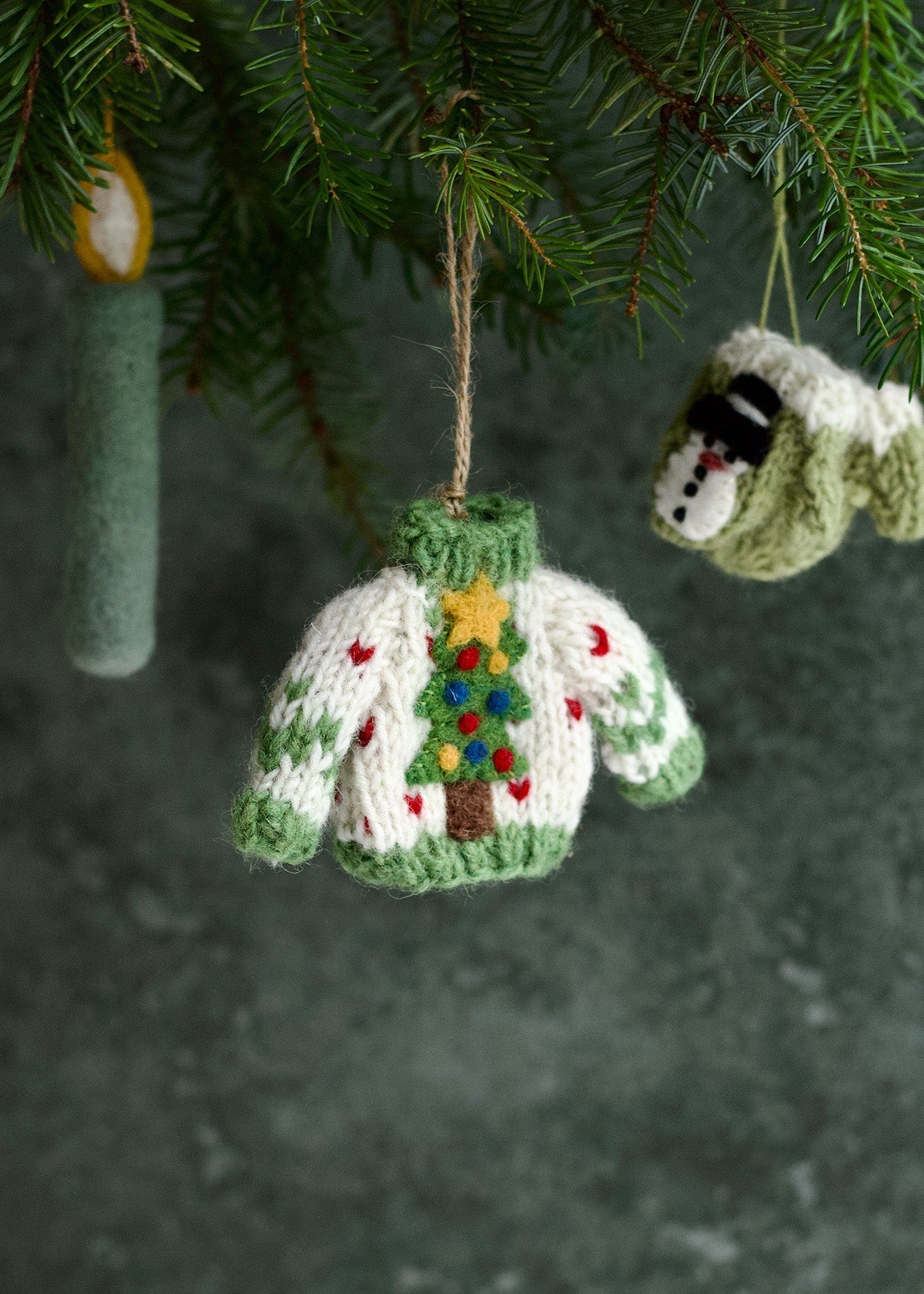 Knitted Christmas sweater ornament with a tree design hanging from a tree.