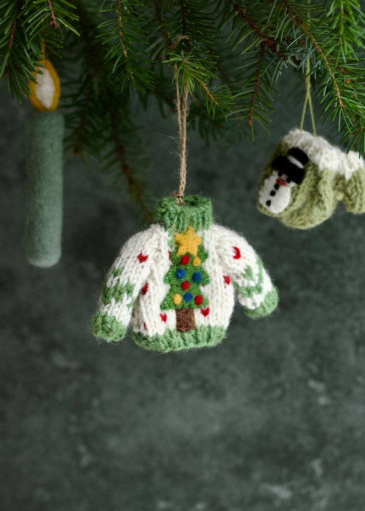 Knitted Christmas sweater ornament with a tree design hanging from a tree.