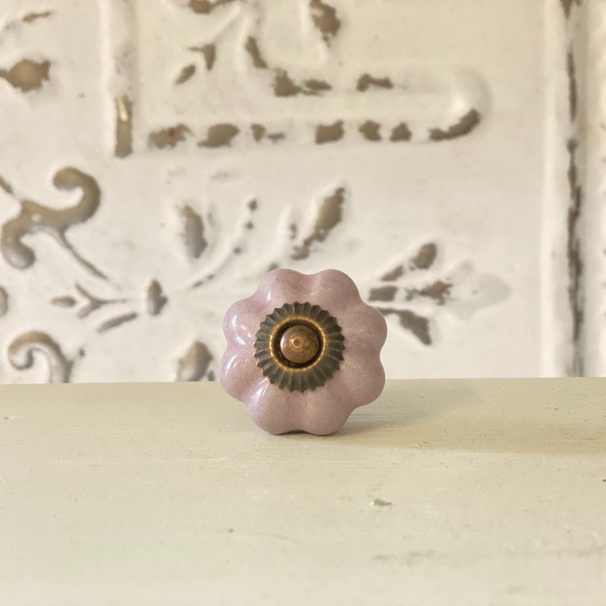 A lilac-colored furniture knob with a metallic base, placed against a white background with a decorative pattern.