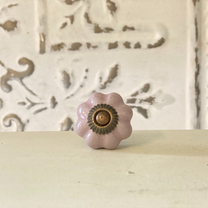 A lilac-colored furniture knob with a metallic base, placed against a white background with a decorative pattern.