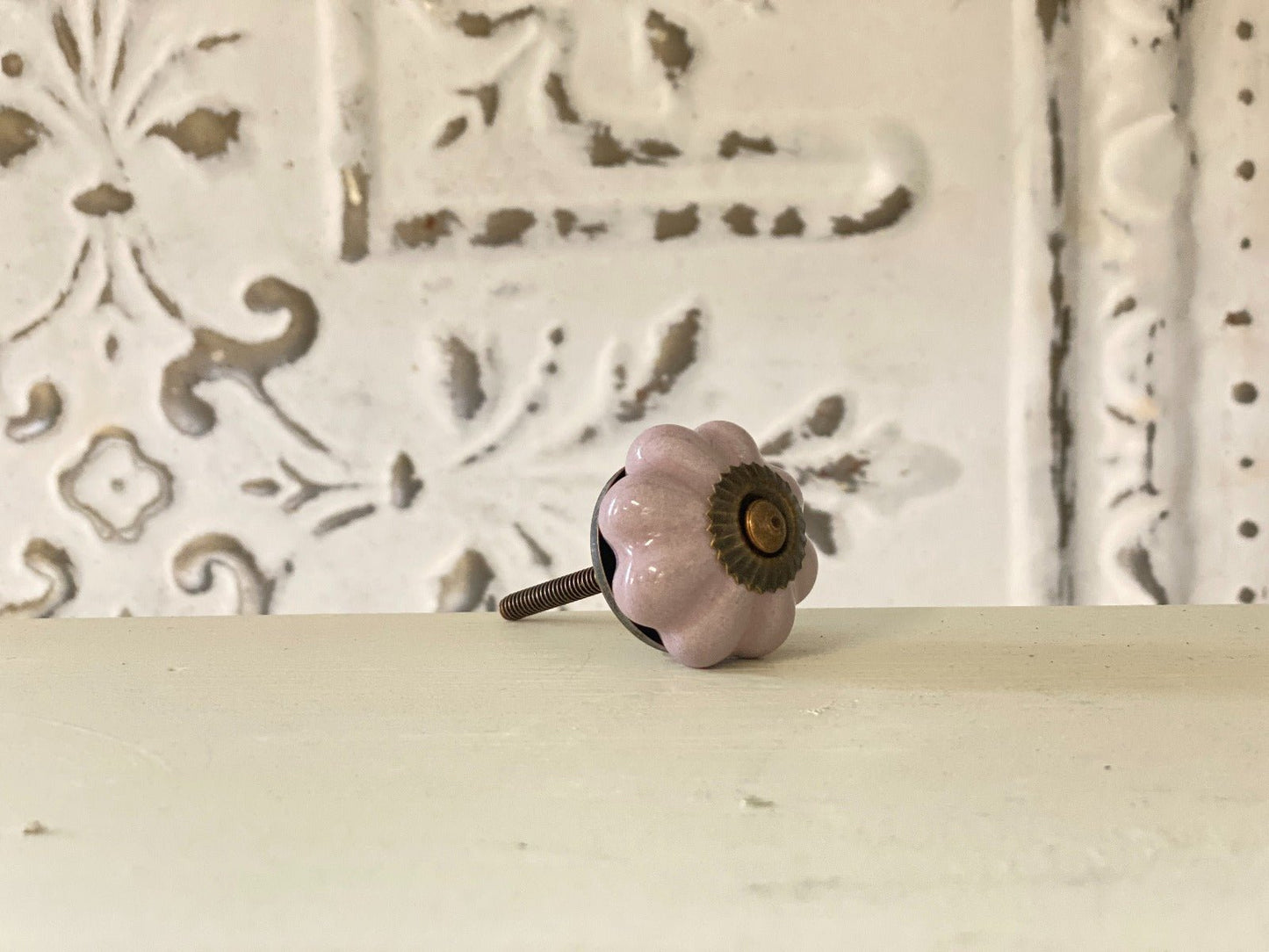A lilac-colored furniture knob with a metallic base, placed against a white background with a decorative pattern.