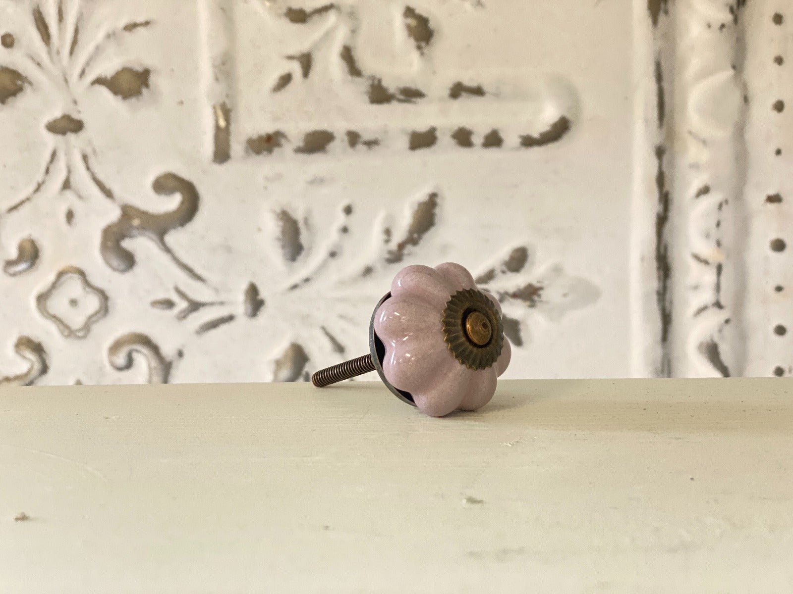 A lilac-colored furniture knob with a metallic base, placed against a white background with a decorative pattern.
