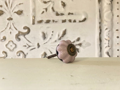 A lilac-colored furniture knob with a metallic base, placed against a white background with a decorative pattern.