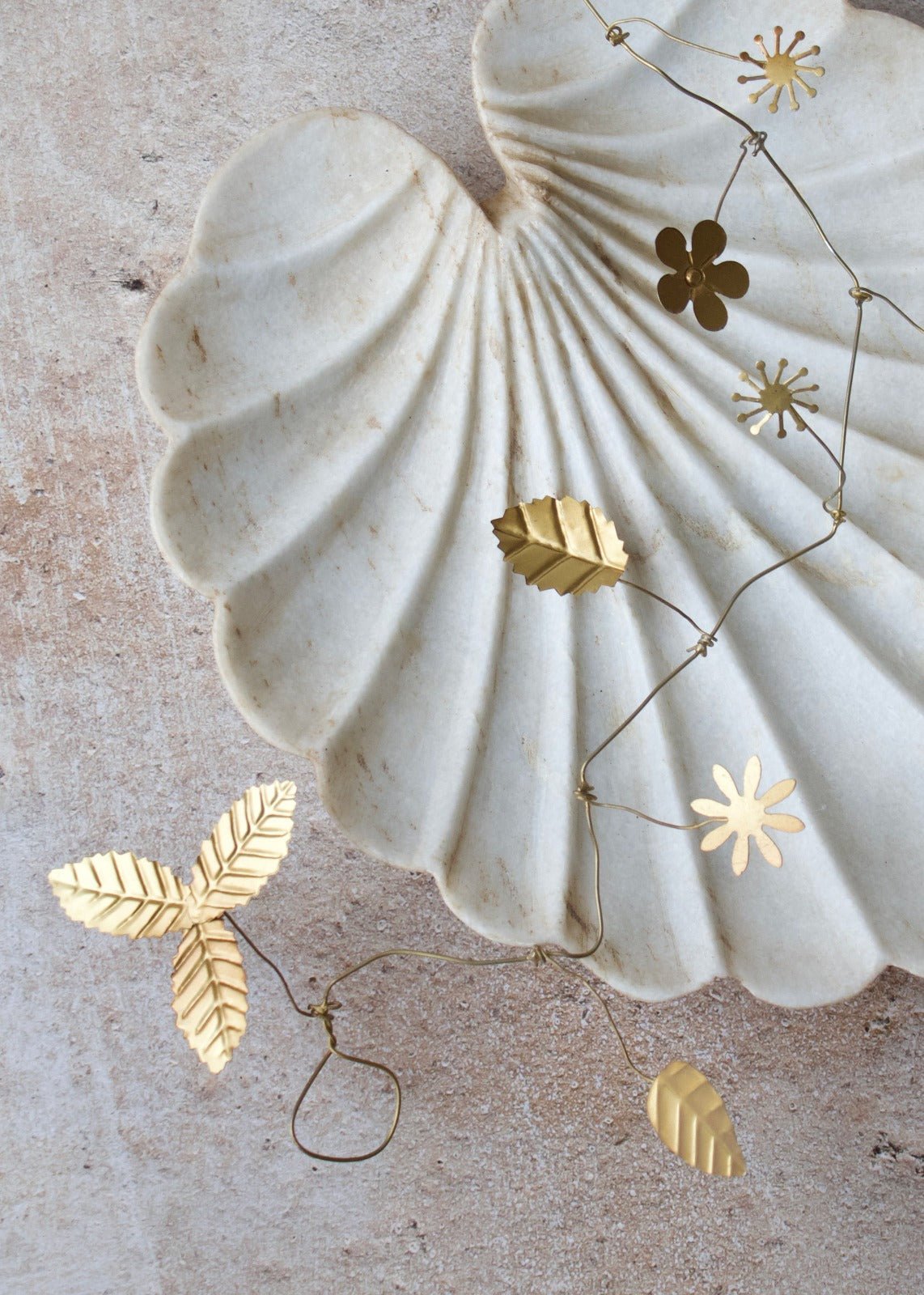 Gold leaf earrings on a textured beige surface with a shell in the background