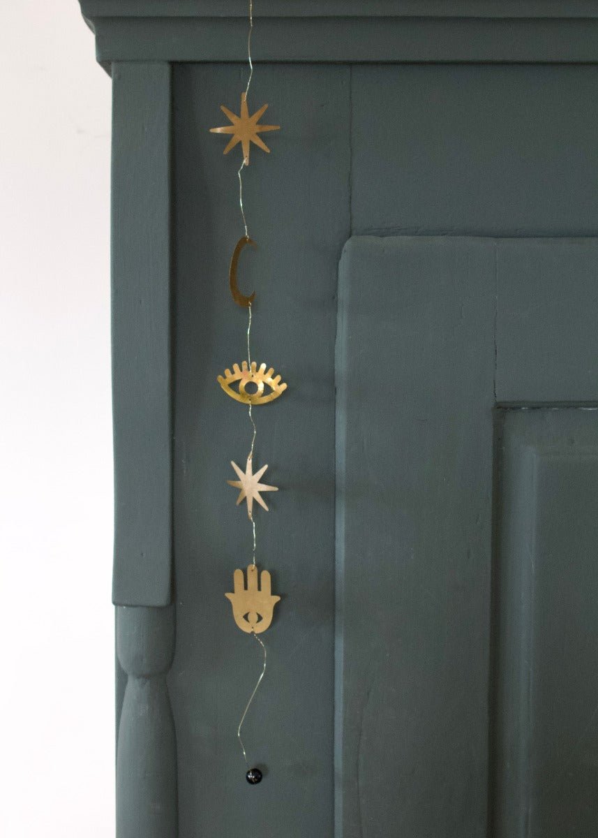 Decorative string with star, eye, and hand of Fatima symbols on a dark green wall.