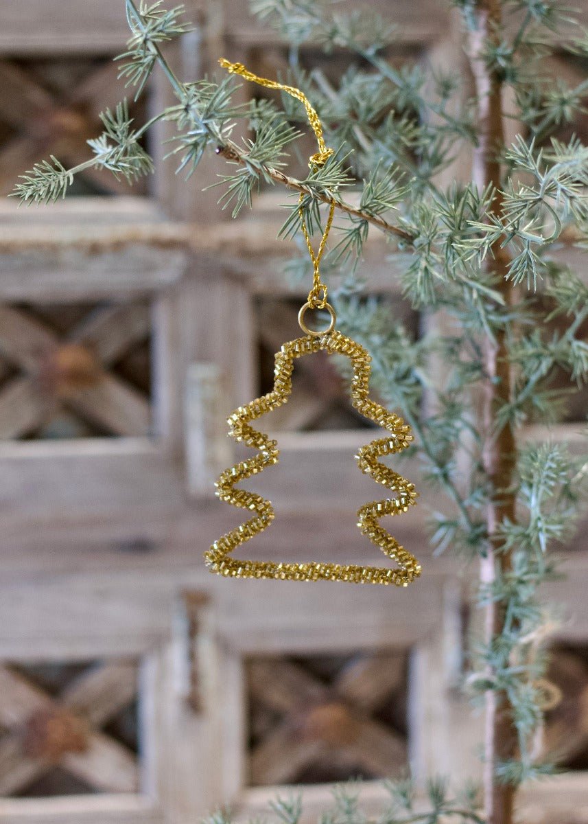 Gold zigzag ornament hanging on a Christmas tree branch with a rustic wooden background.