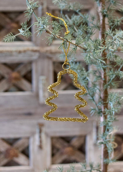 Gold zigzag ornament hanging on a Christmas tree branch with a rustic wooden background.
