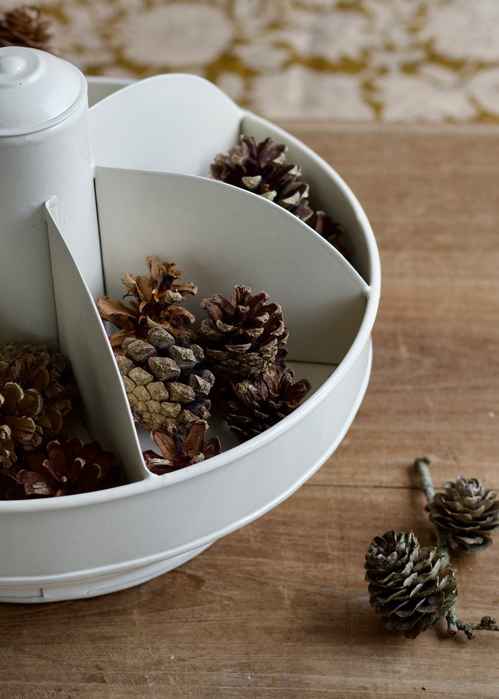White decorative bowl filled with pine cones on a wooden surface