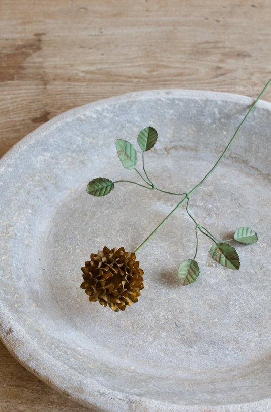 Handmade brown wirework flower stem with layered metal petals and green wire leaves lying in a stone bowl.