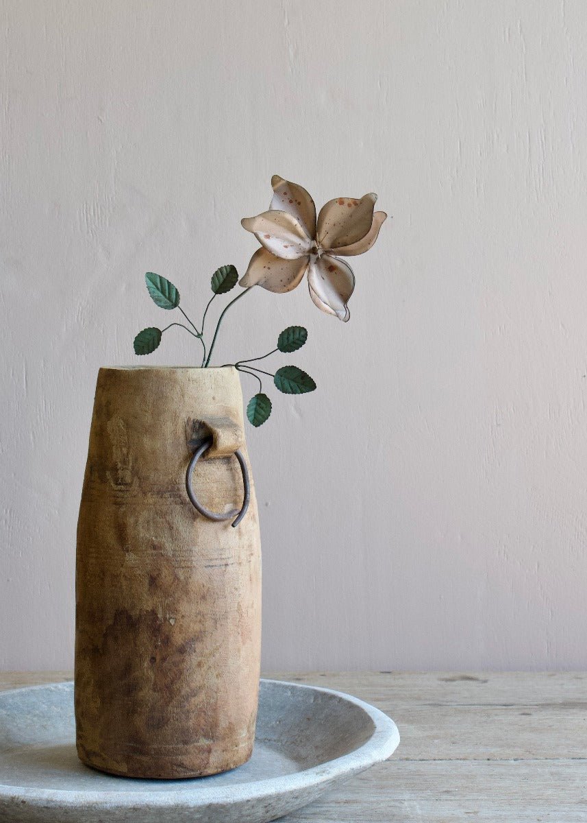 Handmade metal flower with curved petals and green leaves, displayed in a rustic wooden vase on a wooden table.