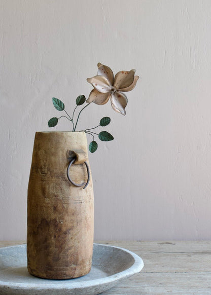 Handmade metal flower with curved petals and green leaves, displayed in a rustic wooden vase on a wooden table.