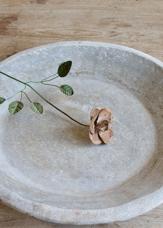 Handmade metal rose flower with green leaves and rustic patina, displayed inside a stone bowl.