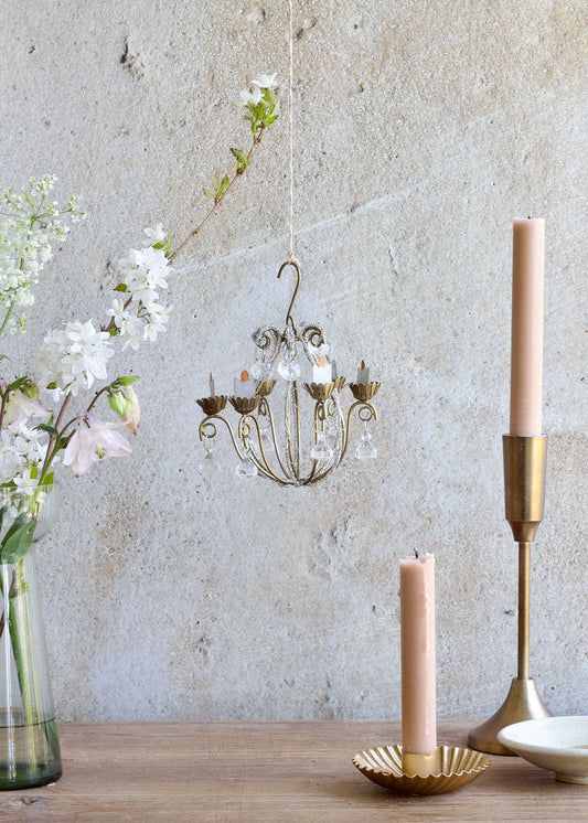 Decorative chandelier with flowers and candles on a wooden surface against a textured wall.