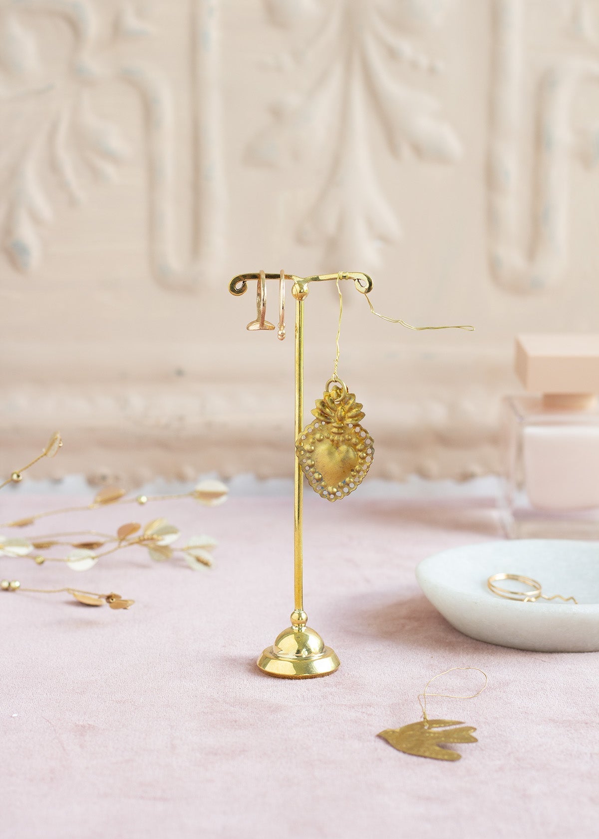 Gold earring stand with heart-shaped earrings on a pink surface