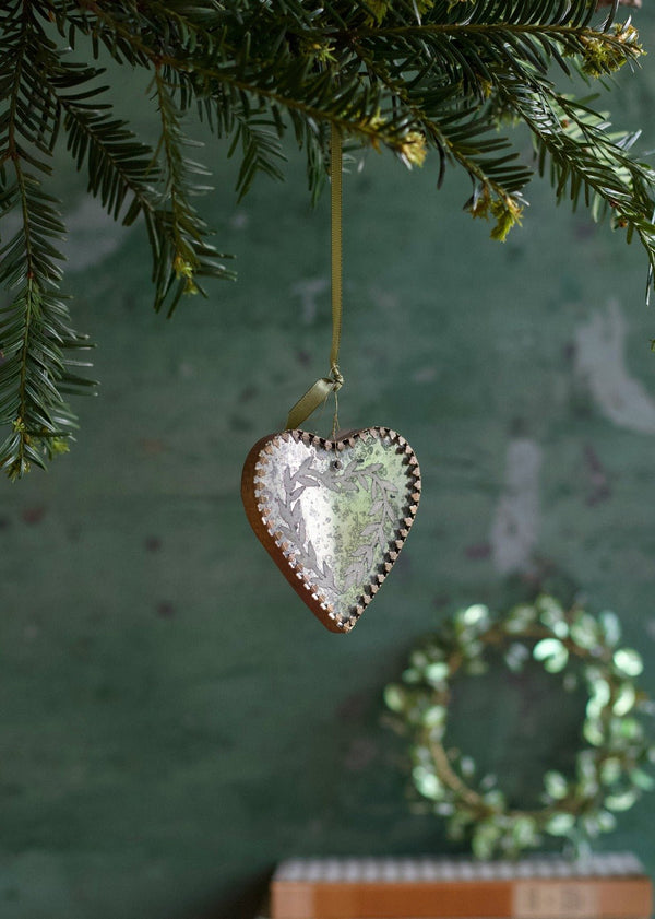 Antique-style silvered glass heart ornament with leaf details, hanging on a fir branch.