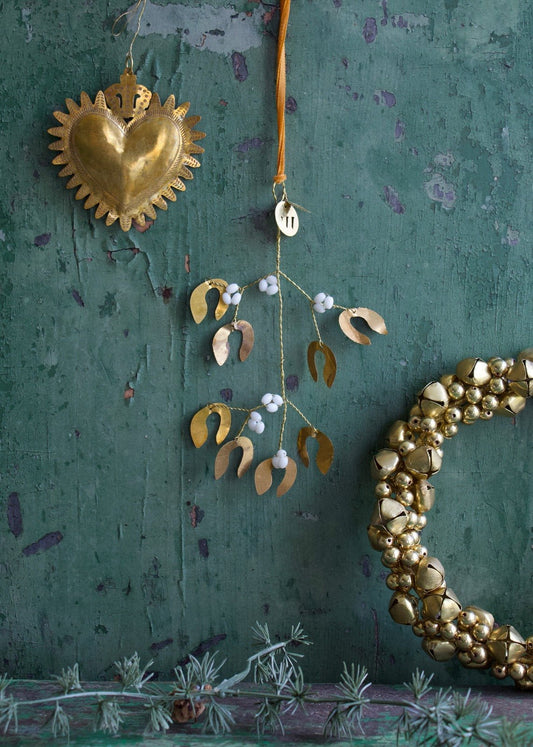 A decorative mistletoe bunch with pearl beads and gold-colored heart-shaped ornaments hanging against a green textured background.
