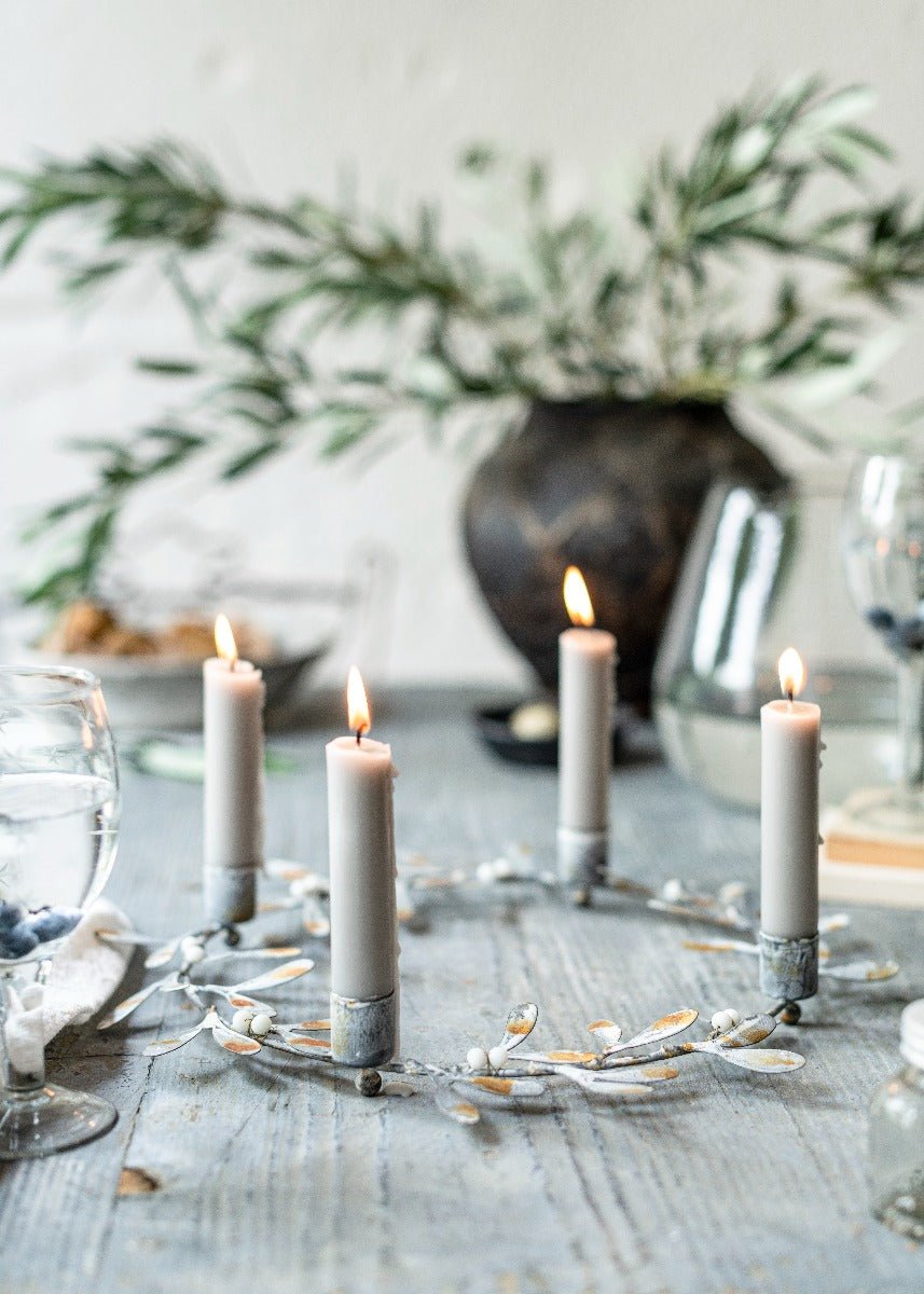 Candlelit table setting with candles and greenery on a neutral background