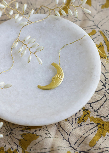 Gold crescent moon necklace on a marble surface with a floral patterned fabric underneath.