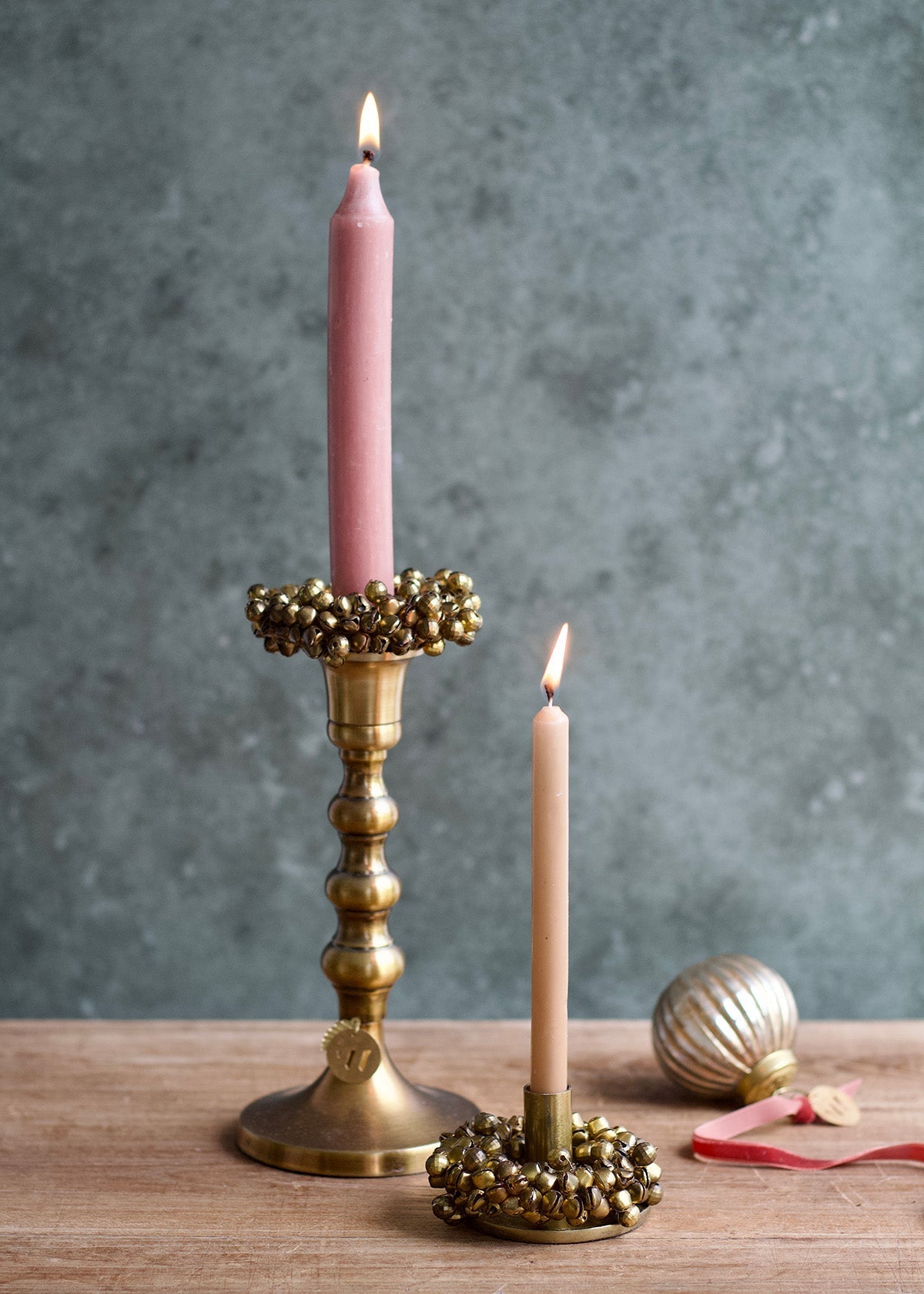 Pink candles in gold candlesticks on a wooden surface with a gray background