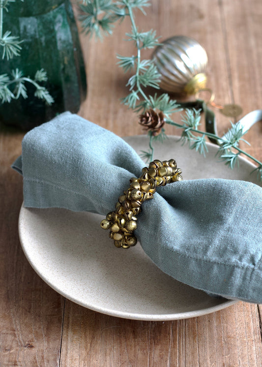 Gold beaded napkin ring on a light blue napkin with a white plate and decorative elements on a wooden surface.