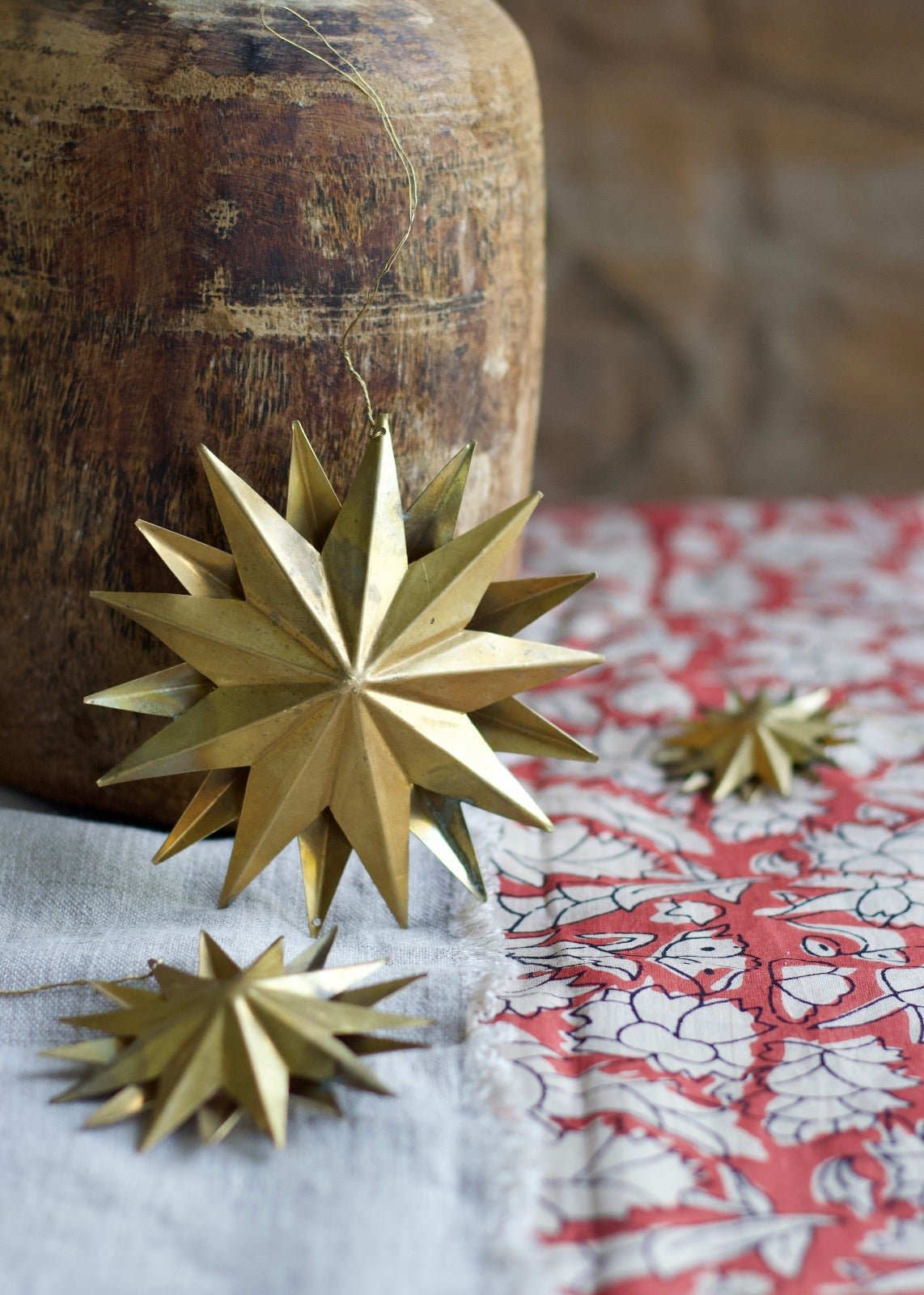 Three-dimensional brass star ornament with a radiant geometric design, displayed on a linen cloth with red floral print.

