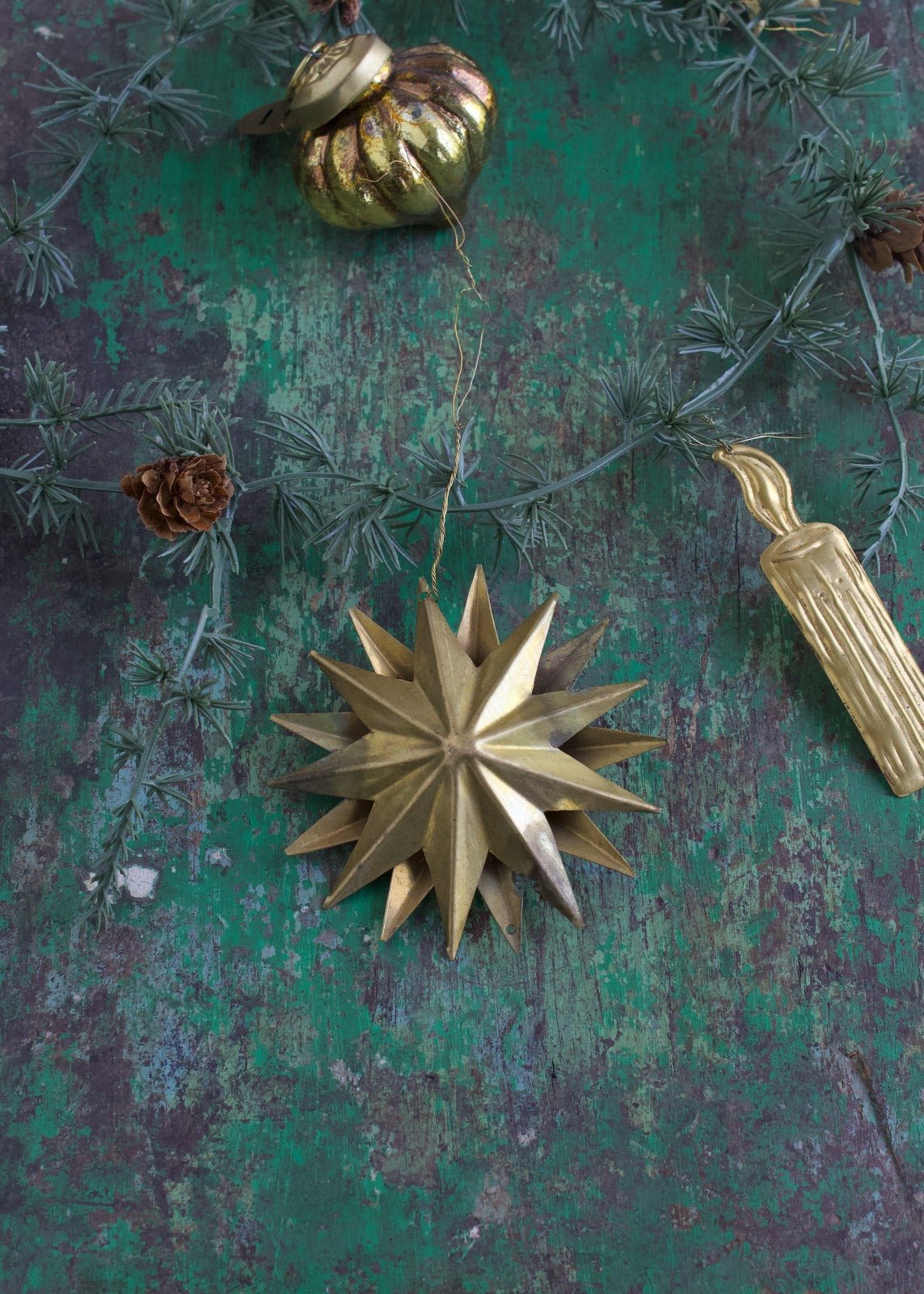 Brass 3D star ornament with multiple pointed rays, hanging on a rustic green background with pine branch and other vintage decorations.