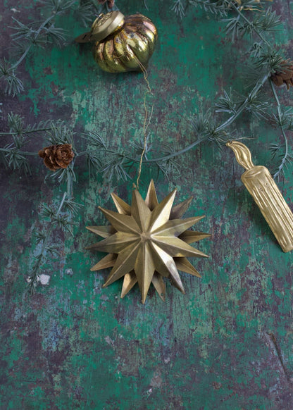 Brass 3D star ornament with multiple pointed rays, hanging on a rustic green background with pine branch and other vintage decorations.