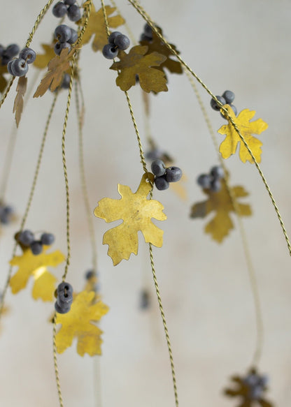 Close-up of brass oak leaves and grey beads hanging from twisted brass wire strands.