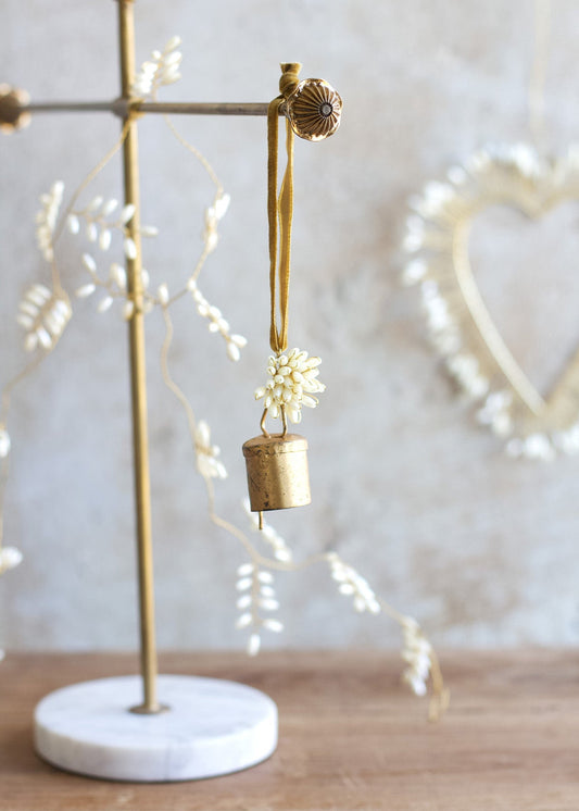 Brass bell with floral decoration on a marble stand against a neutral background