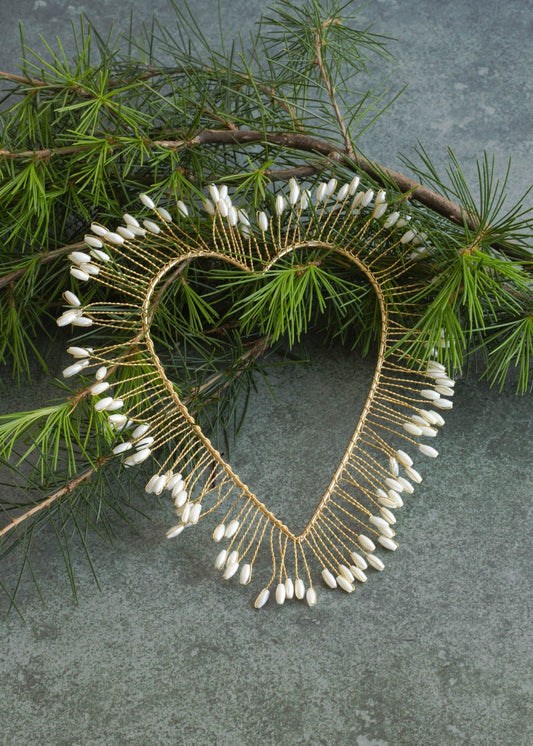Heart-shaped necklace with white beads on a branch with green leaves