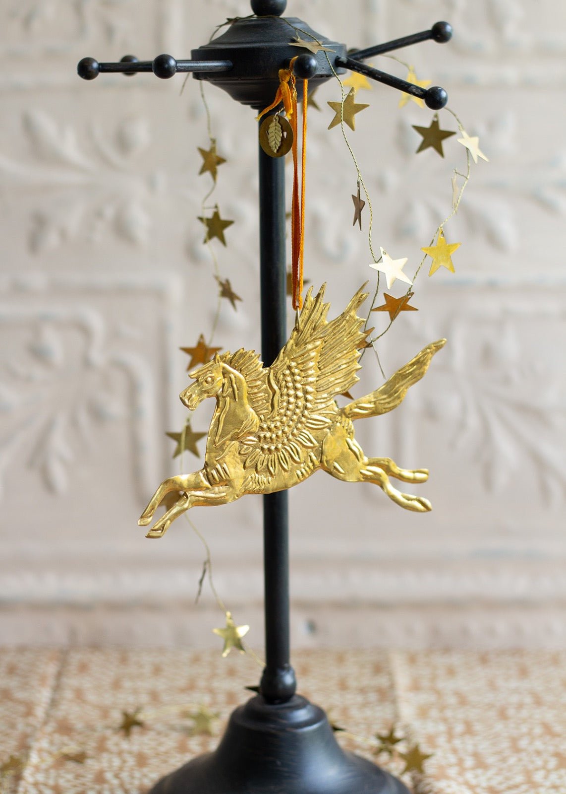 Gold brass Pegasus ornament with detailed wings, hanging from a velvet ribbon.