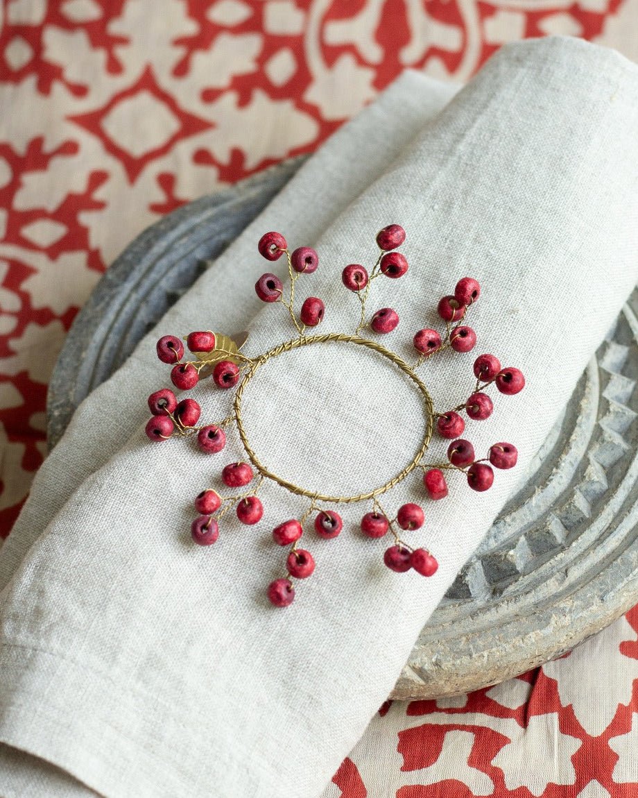Decorative napkin ring with red berries on a folded white napkin over a patterned tablecloth.