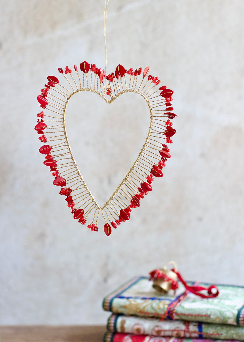 Heart-shaped decorative item with red beads on a neutral background
