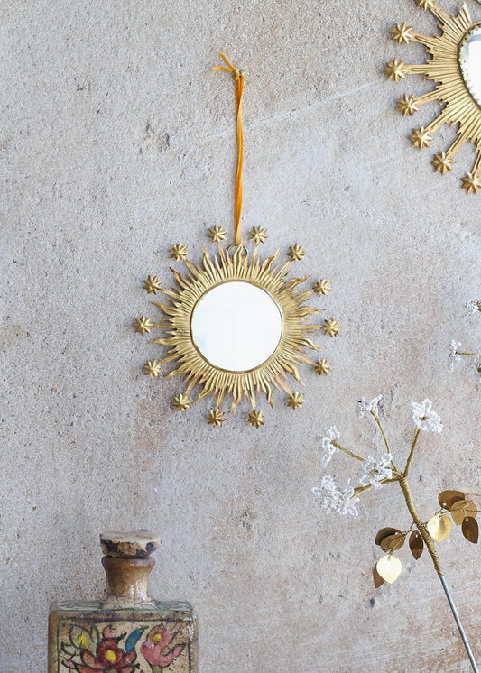 Decorative gold sun-shaped mirror hanging on a textured wall with a vase and flowers.