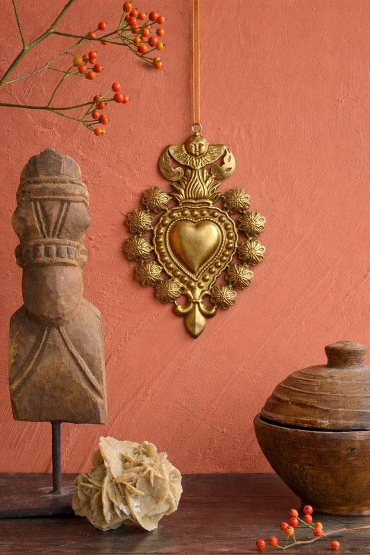 Decorative wall hanging with heart design, wooden sculpture, and pot against a pink wall.