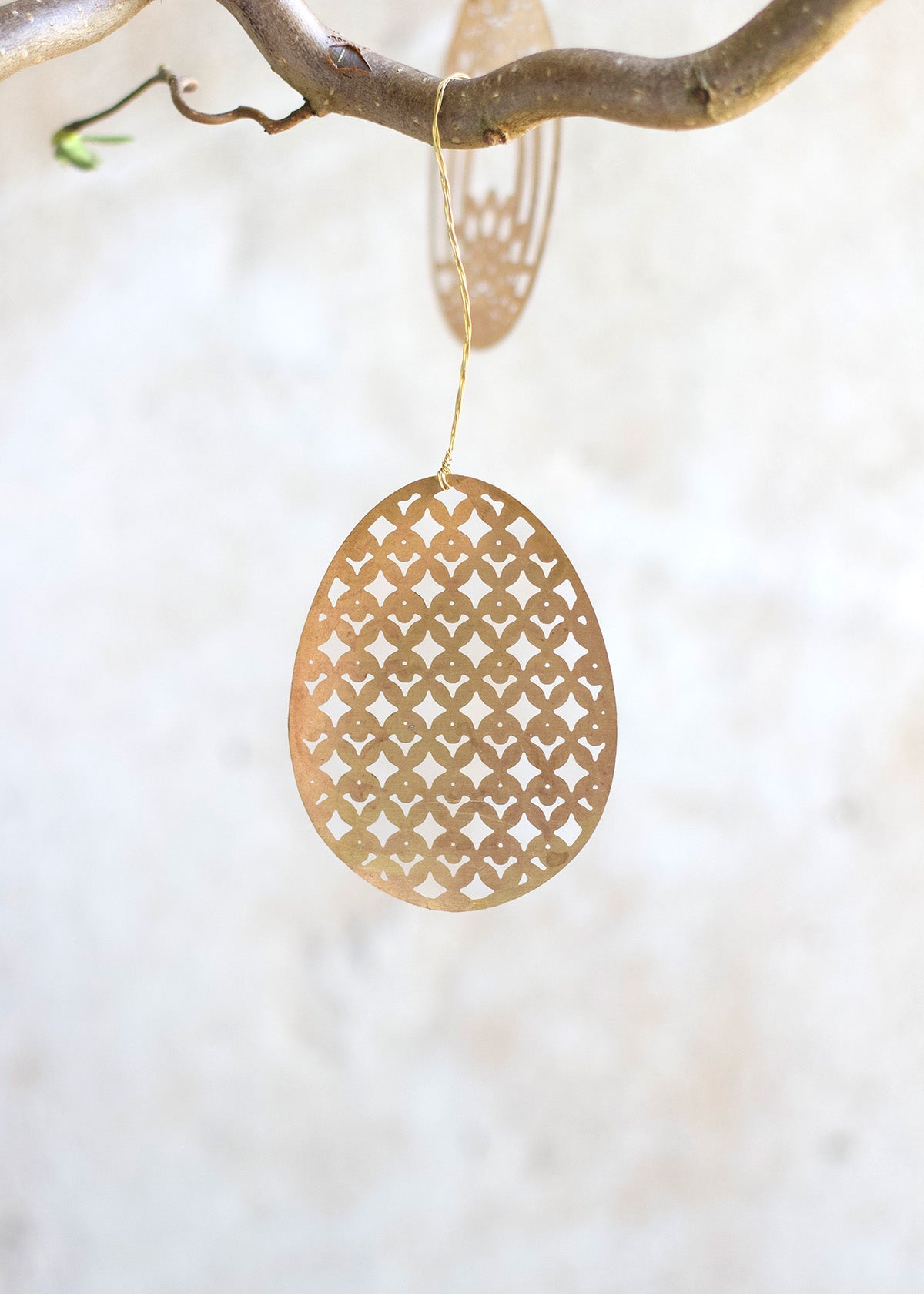 Gold geometric pendant hanging from a branch on a white background