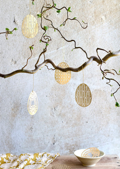 Decorative eggs hanging from a branch against a textured wall.