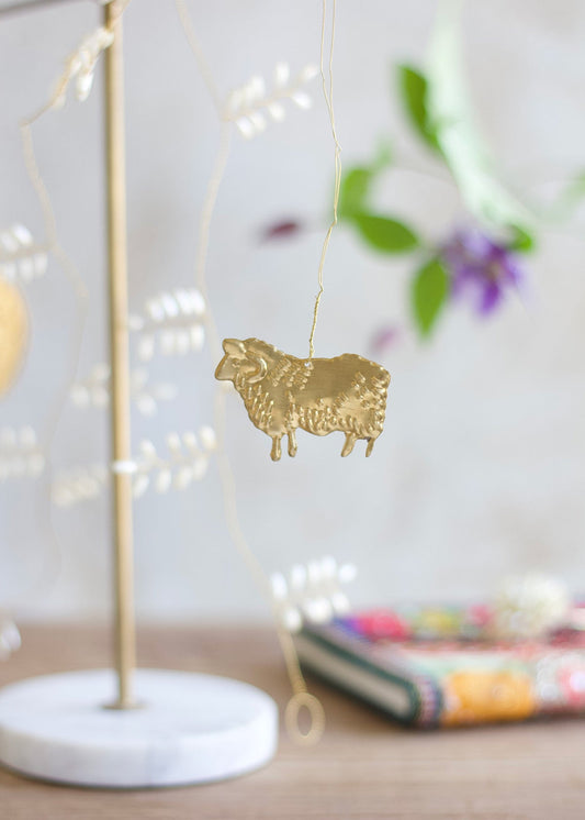Brass sheep ornament hanging from a delicate garland with a white marble base and floral background.