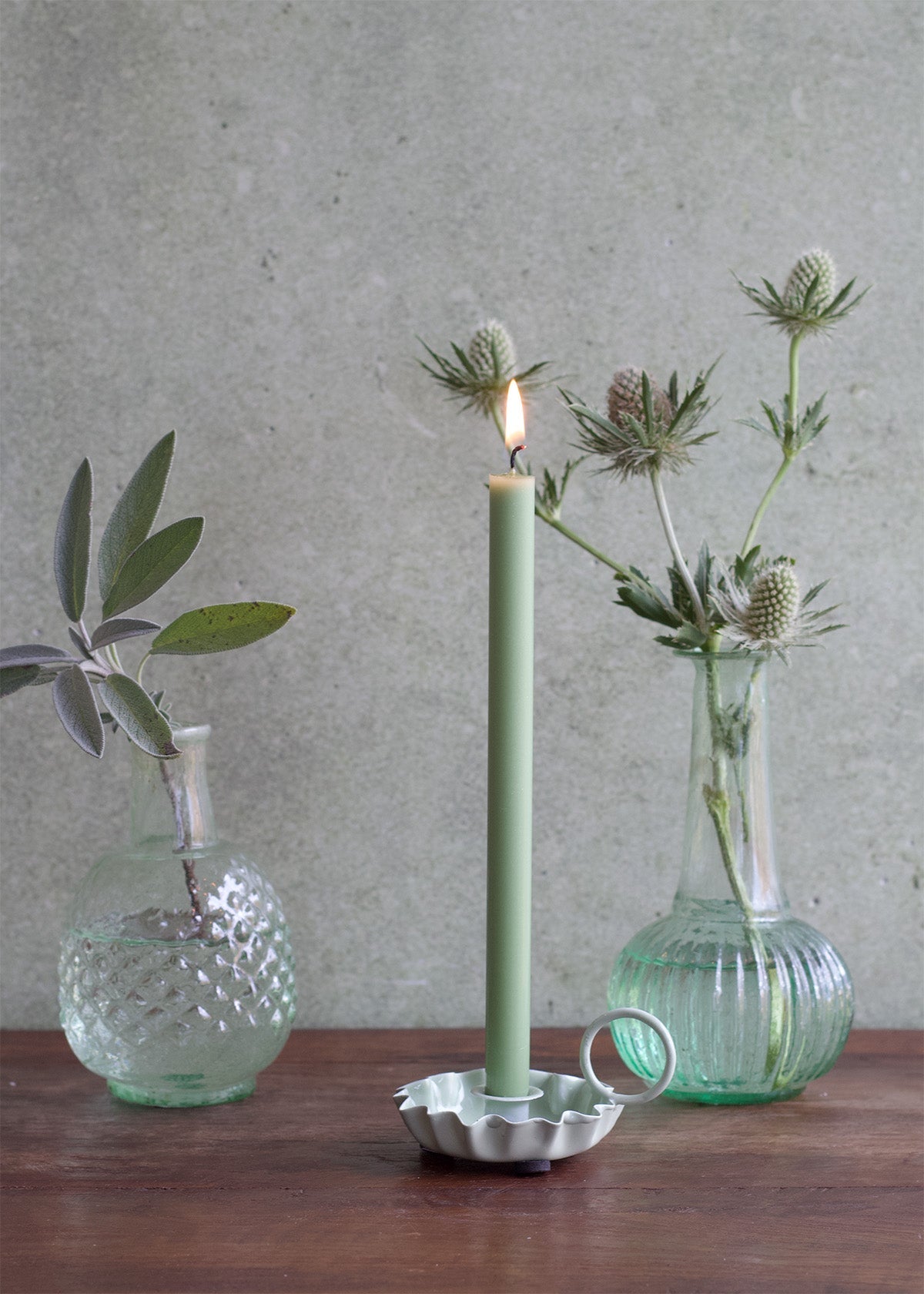 Candle with decorative holder on a wooden surface with two glass vases containing plants.
