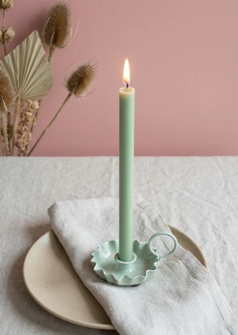 Light green candle in a decorative holder on a white plate with a pink background