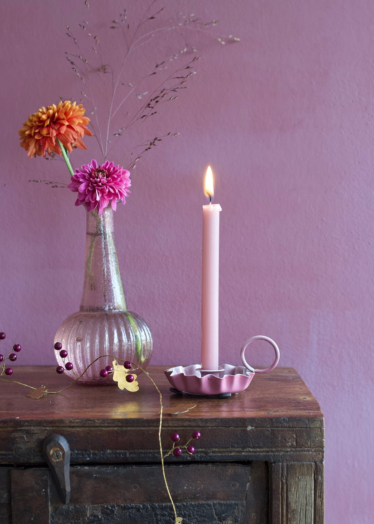 Vase with flowers and candle on a wooden surface against a purple wall