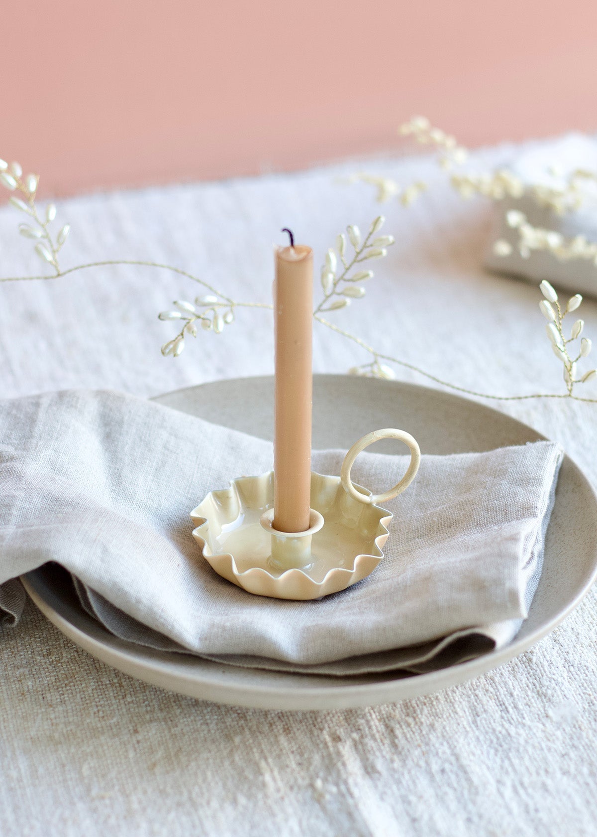 Candle in a decorative holder on a white plate with a light pink background