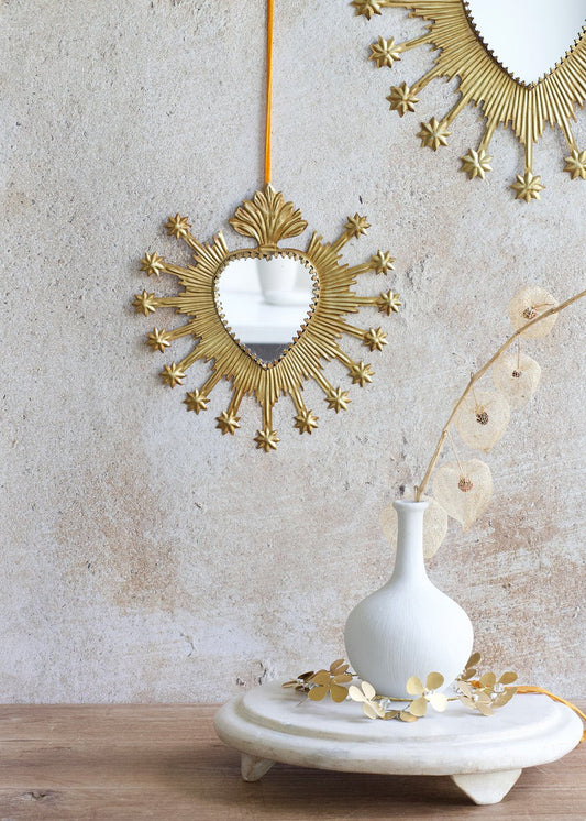 Decorative gold mirror with a white vase and small plant on a wooden surface.