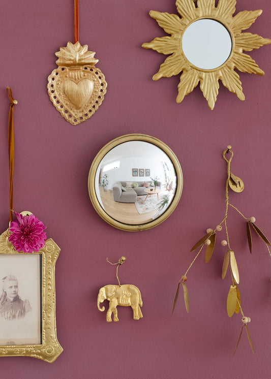 Decorative wall with gold mirrors, frames, and a sun-shaped mirror on a purple wall.