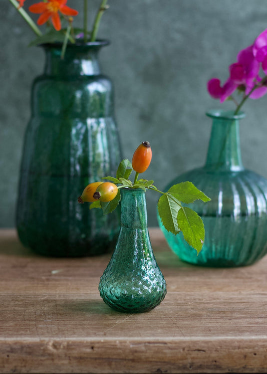 Three green glass vases with floral arrangements on a wooden surface.