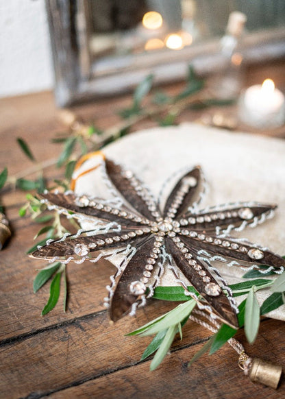 Decorative star-shaped object with embellishments on a wooden surface with greenery